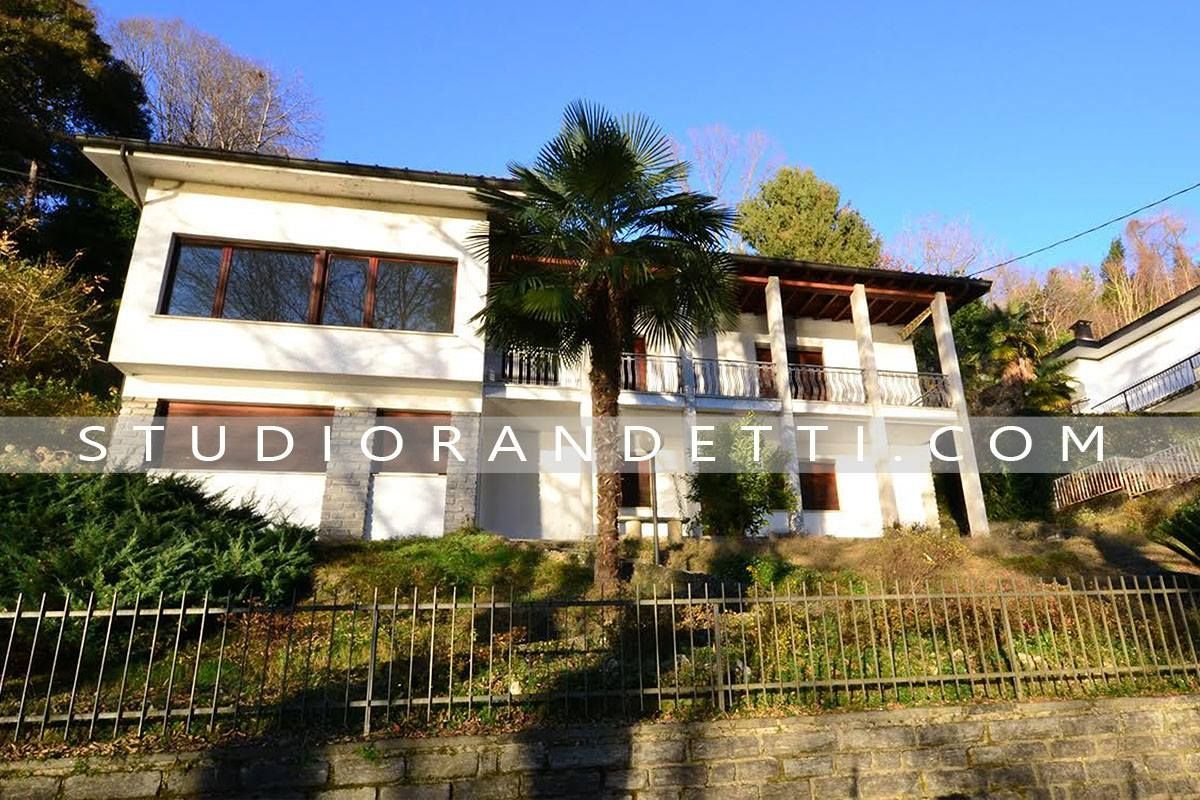 Edificio bianco sulla collina con tetto rosso, balconi e vegetazione sotto un cielo azzurro limpido.