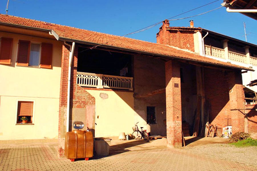 Casa in mattoni illuminata dal sole con tetto di tegole rosse, balcone e due scooter parcheggiati davanti.