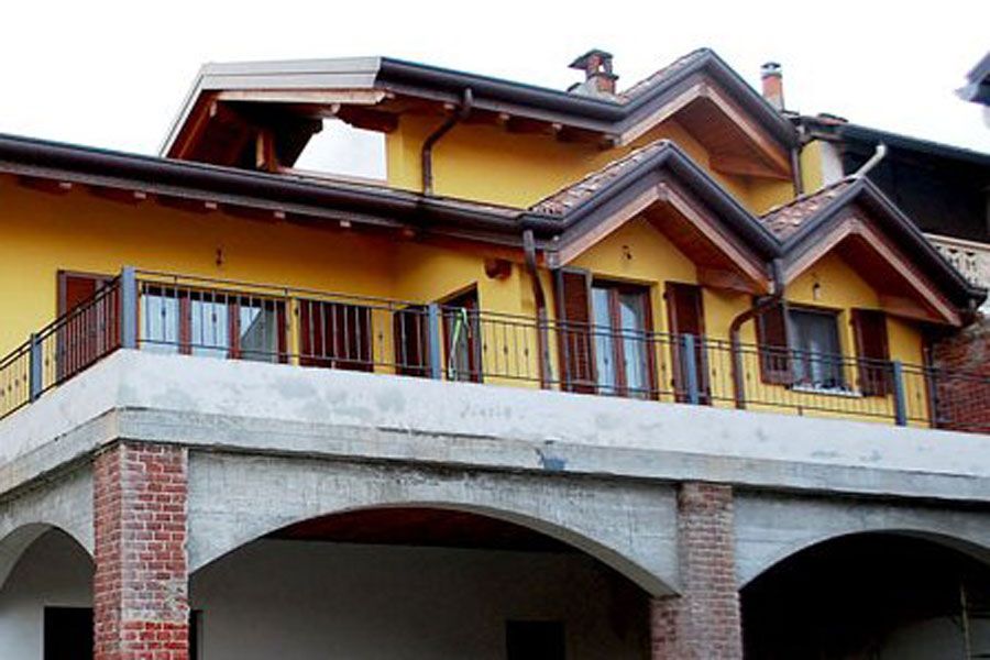 Casa gialla con balconi rossi e supporti in cemento ad arco sotto la linea del tetto.
