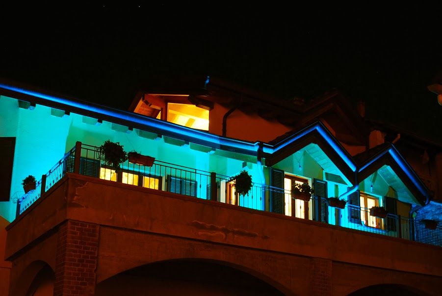 La facciata dell'edificio, illuminata di notte, risplende di tonalità blu e arancioni contro un cielo scuro.