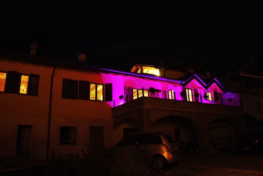 Casa di notte illuminata da luci rosa acceso e giallo caldo, con un'auto parcheggiata davanti