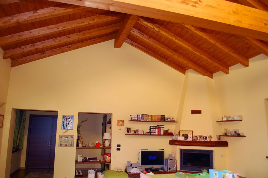 Soggiorno con soffitto a volta in legno, pareti beige, porta, scrivania e mensole per TV/camino.