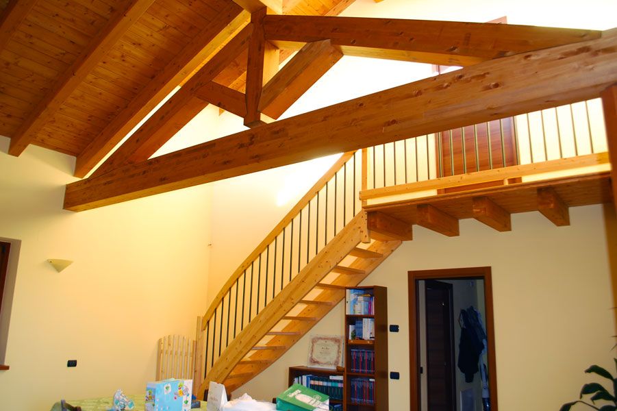 Scala in legno e soppalco in una casa luminosa con travi a vista e pareti color crema.
