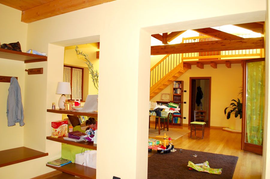 Un corridoio luminoso con scale in legno, scaffali a vista e una porta che conduce a una stanza accogliente con giocattoli sul pavimento.