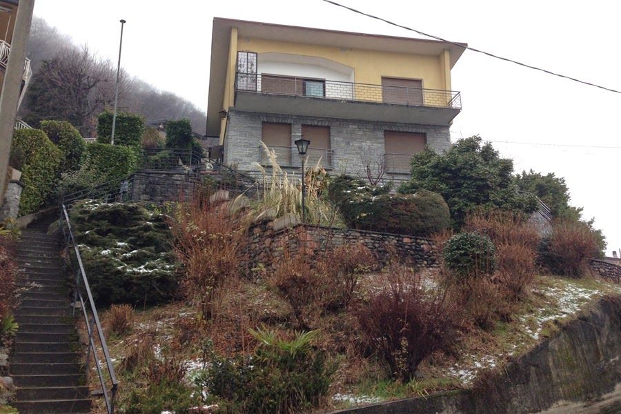 Casa su un ripido pendio con arbusti e cielo nuvoloso