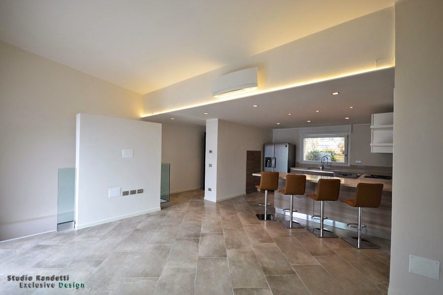 Cucina e zona giorno moderne a pianta aperta con pavimento piastrellato, sgabelli sull'isola e faretti a incasso sul soffitto.