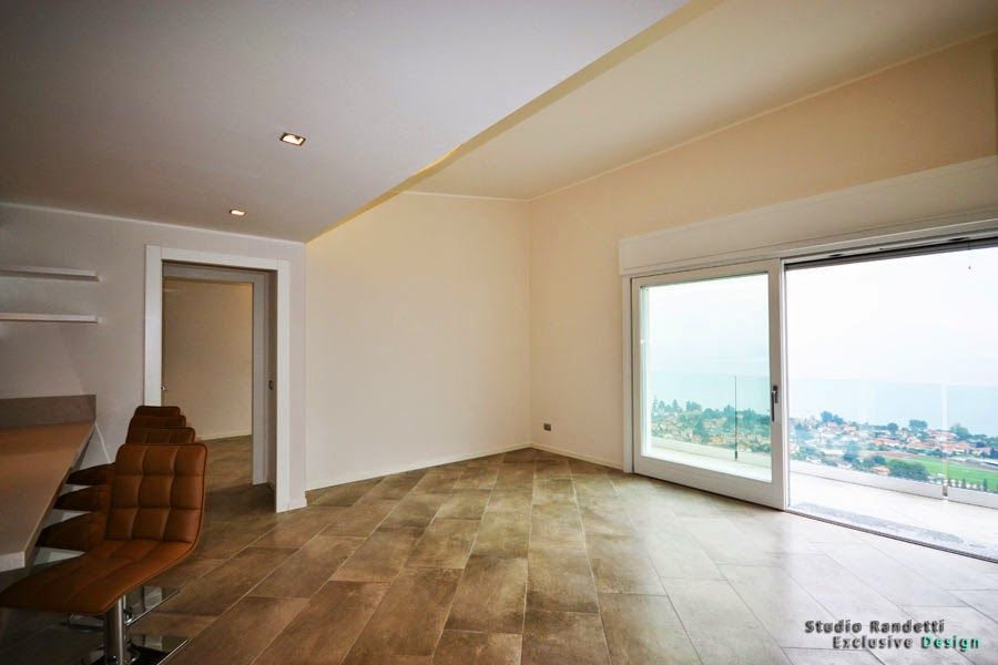 Ampia stanza vuota con pavimento piastrellato, soffitto inclinato e grandi porte scorrevoli in vetro con vista sulla città.