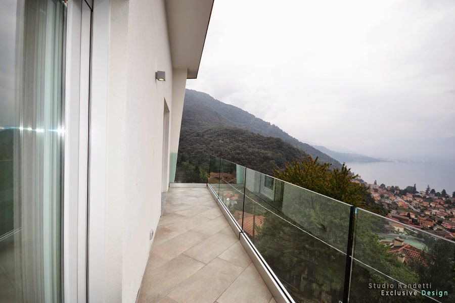 Balcone con ringhiera in vetro affacciato su una montagna nebbiosa e su una cittadina costiera sotto un cielo nuvoloso.