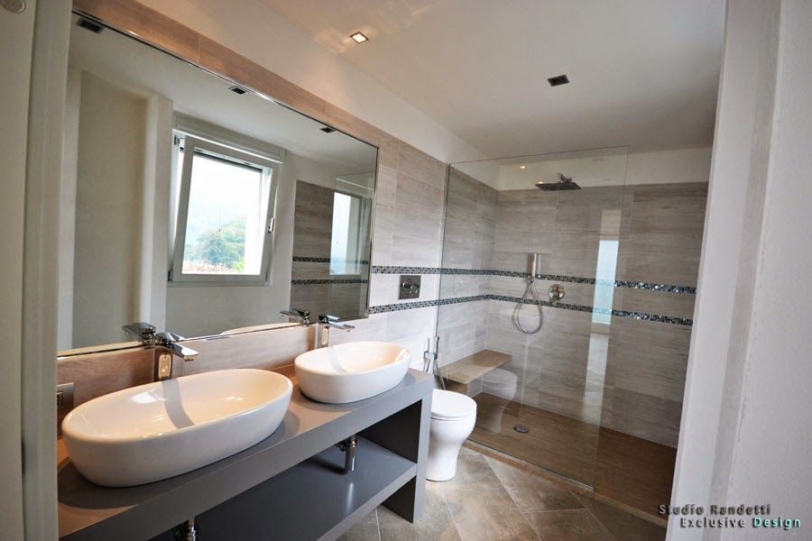 Bagno moderno con doppio lavabo a ciotola, ampio specchio e zona doccia piastrellata.