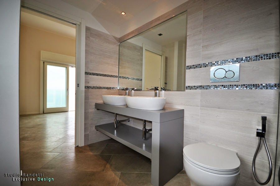 Bagno moderno con doppio lavabo, ampio specchio, WC e pareti rivestite con piastrelle beige.