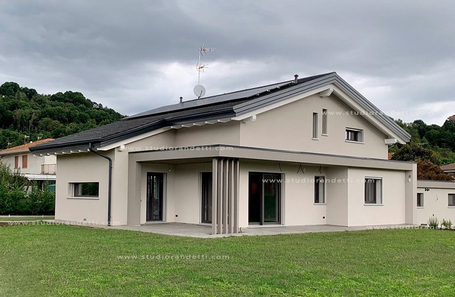 Casa beige a un solo piano con tetto scuro e prato verde antistante, vista in una giornata nuvolosa.