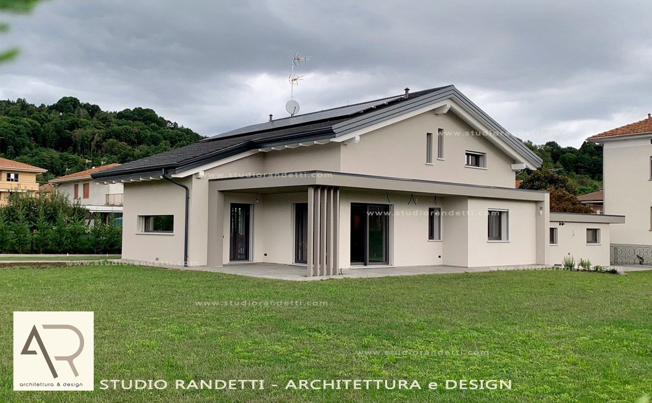 Casa moderna a due piani di colore beige con tetto scuro, ampie finestre e giardino anteriore erboso.