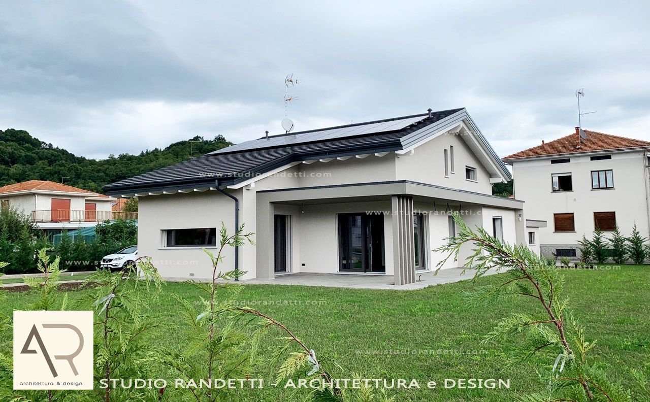 Casa moderna bianca con tetto scuro e grandi finestre in un quartiere residenziale con prato.