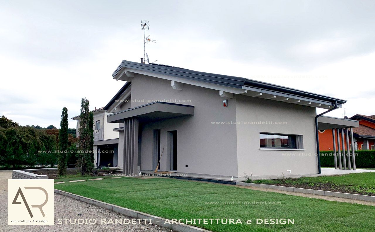 Casa moderna grigia con tetto spiovente, portico anteriore e prato curato sotto un cielo nuvoloso