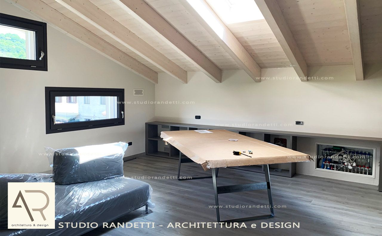 Moderno ufficio mansardato con soffitto inclinato, travi a vista, scrivania in legno, sedia e elemento decorativo a parete simile a un camino.