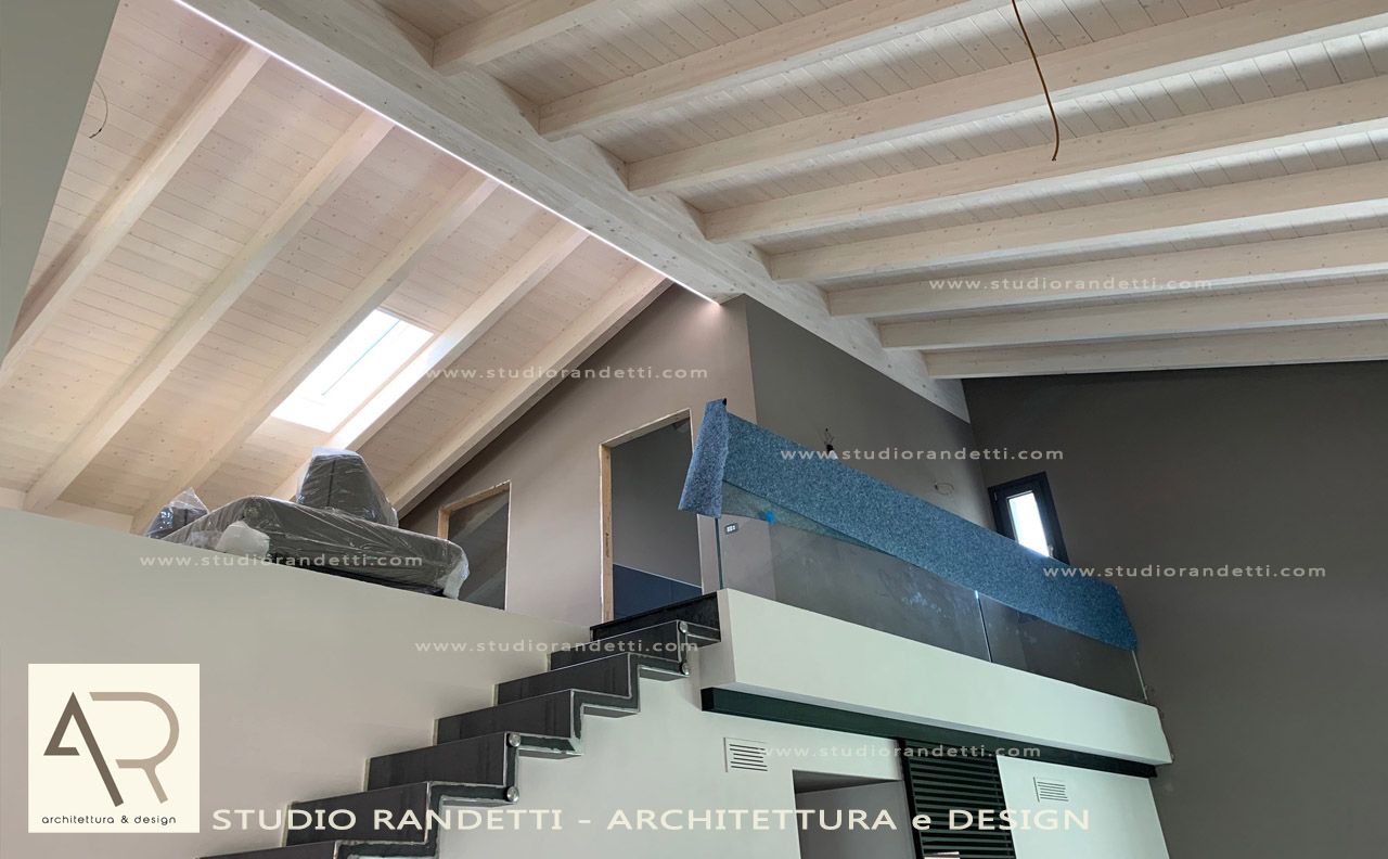 Interno della soffitta con travi in legno a vista, lucernario e mobili o oggetti riposti accatastati lungo la parete.