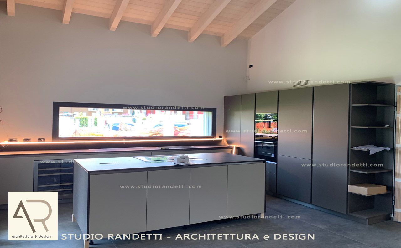 Cucina moderna con soffitto con travi a vista, mobili grigi e un lungo paraschizzi con finestra retroilluminata.