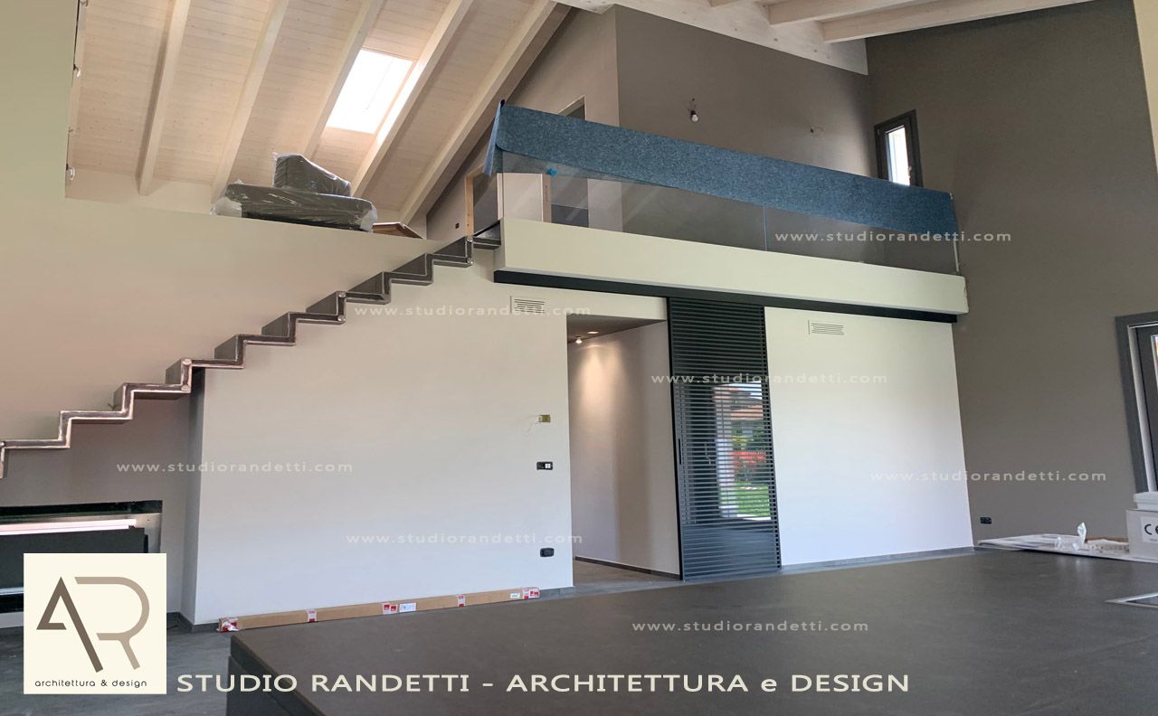 Interno di un loft moderno con scala, soppalco e ampie pareti bianche sotto soffitti inclinati.
