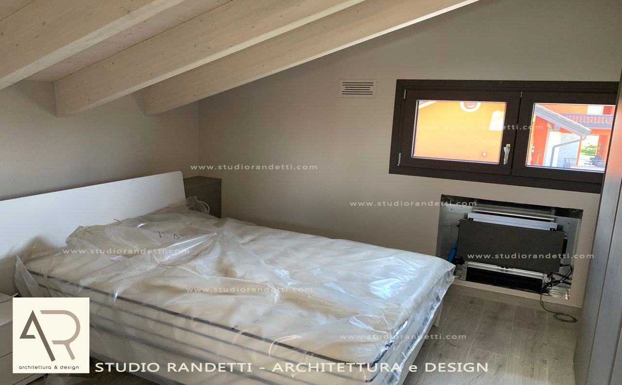Piccola camera da letto in mansarda con letto, soffitto inclinato e finestra sopra un termosifone.