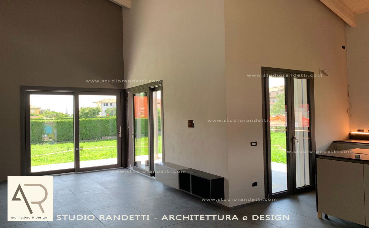 Stanza moderna vuota con pavimento piastrellato, porte a vetri e angolo cottura, illuminata dalla luce naturale proveniente dall'esterno.