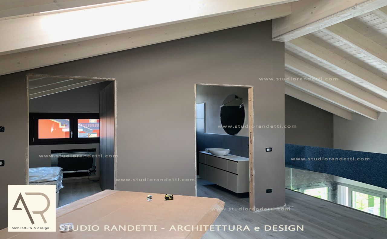 Camera da letto moderna con soffitto inclinato, pareti grigie, letto blu e bagno privato a vista sulla destra.