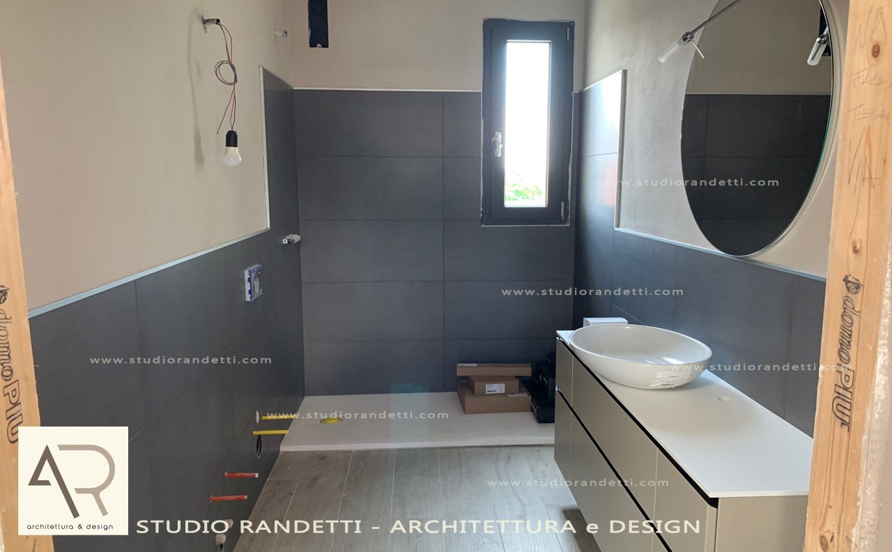 Bagno moderno con pareti grigio scuro, lavabo bianco, doccia e una piccola finestra.