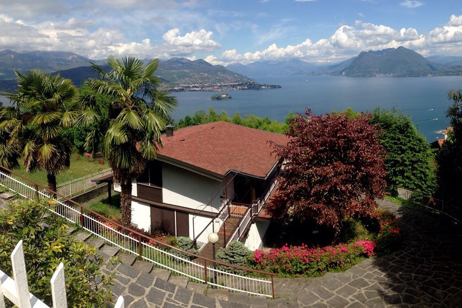 Casa sul lago con tetto rosso, palme e montagne sotto un cielo nuvoloso