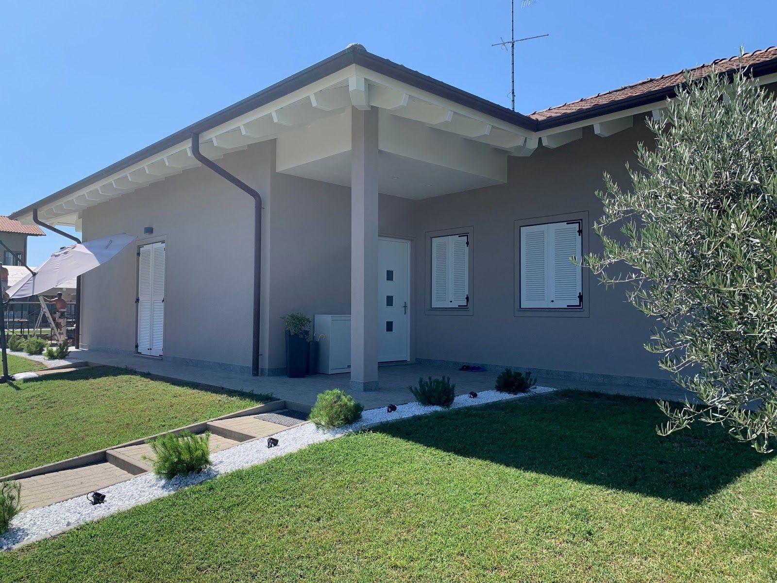 Casa beige a un solo piano con veranda coperta, prato verde e giardino anteriore soleggiato.