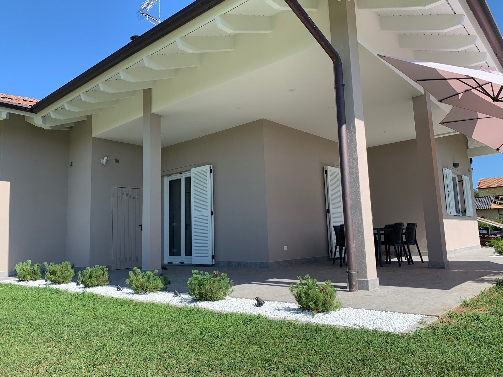 Esterno di una casa moderna con patio coperto, colonne bianche e un piccolo prato.