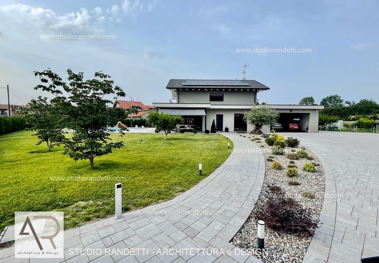 Casa moderna con vialetto d'accesso curvo in pietra, prato verde e giardino con ghiaia sotto un cielo limpido