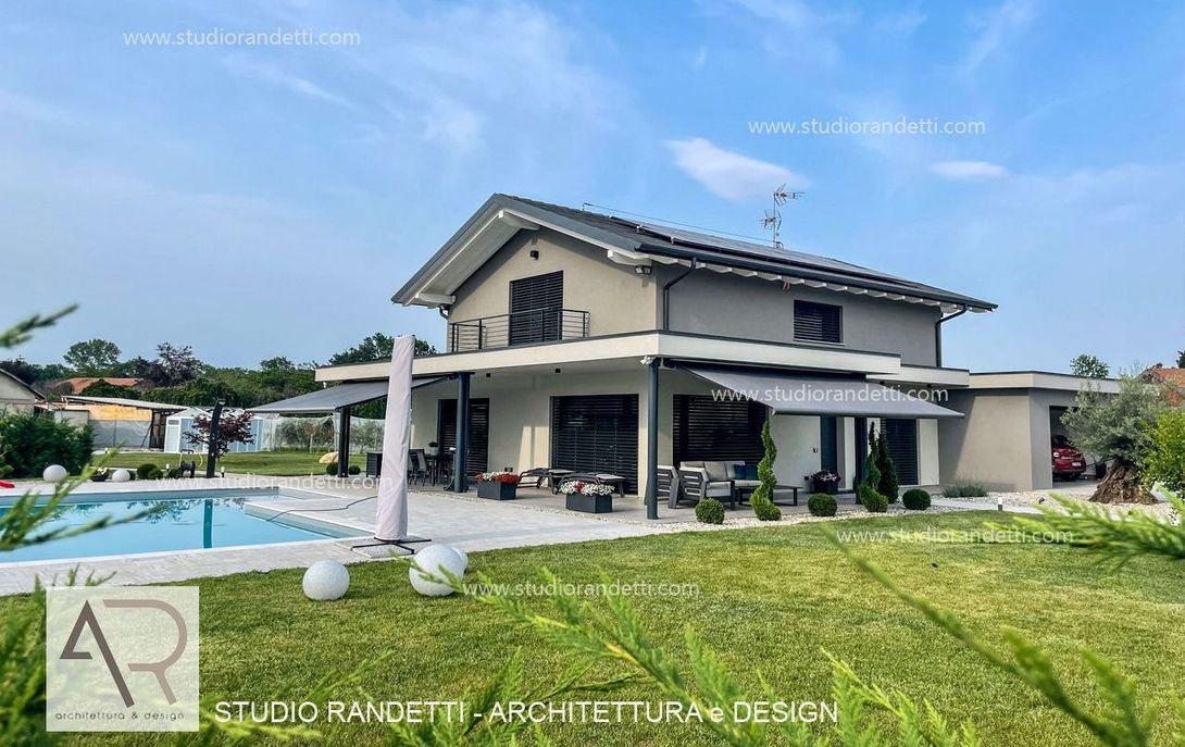 Casa moderna a due piani con piscina, patio e prato verde sotto un cielo azzurro limpido.