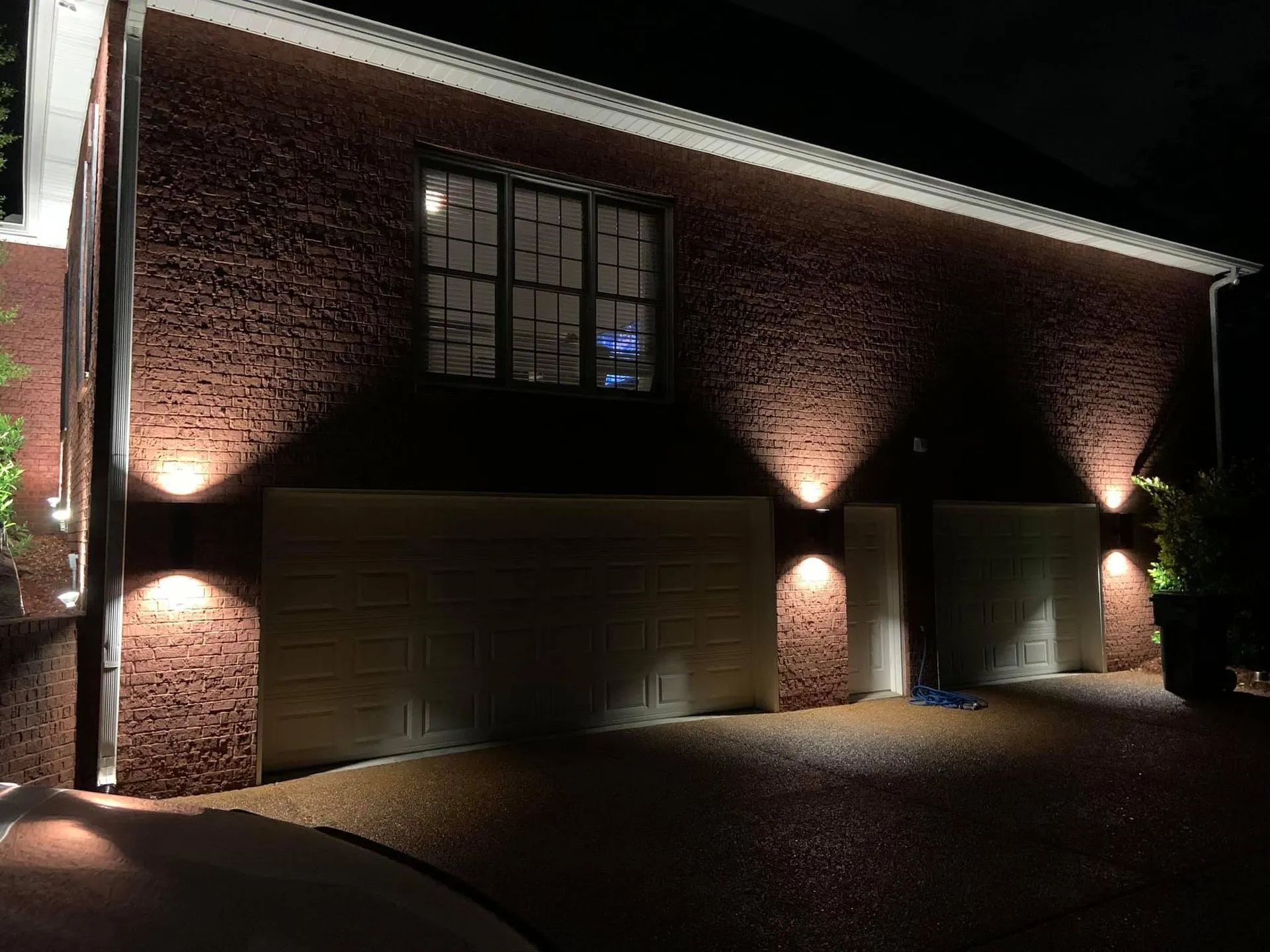 Brick house exterior at night, lit by wall lights and garage doors visible under a dark sky