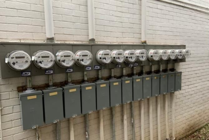 Row of digital electric meters and boxes on a brick wall.