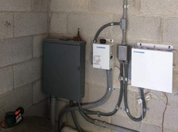 Electrical equipment mounted on a cinder block wall, with conduits and a gray box.