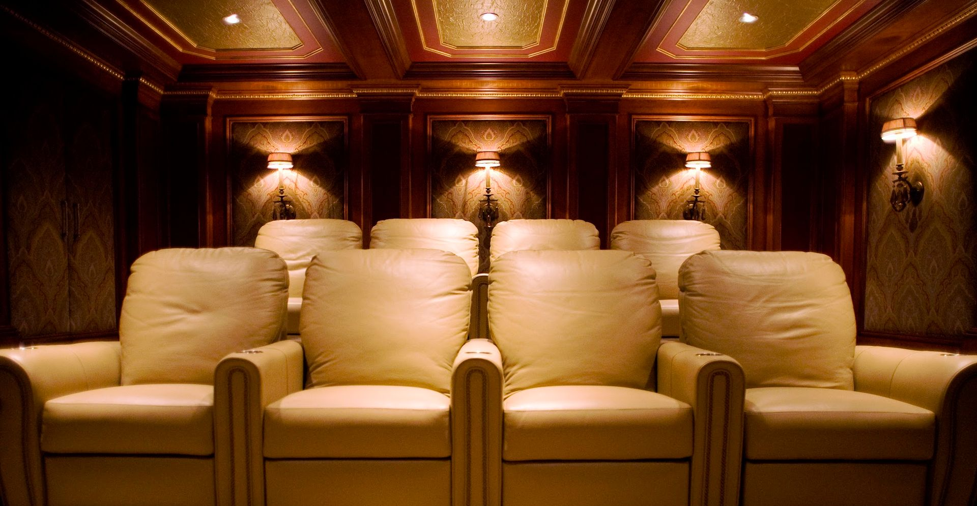 Row of beige theater recliners in a dim, wood-paneled room with warm ceiling lights