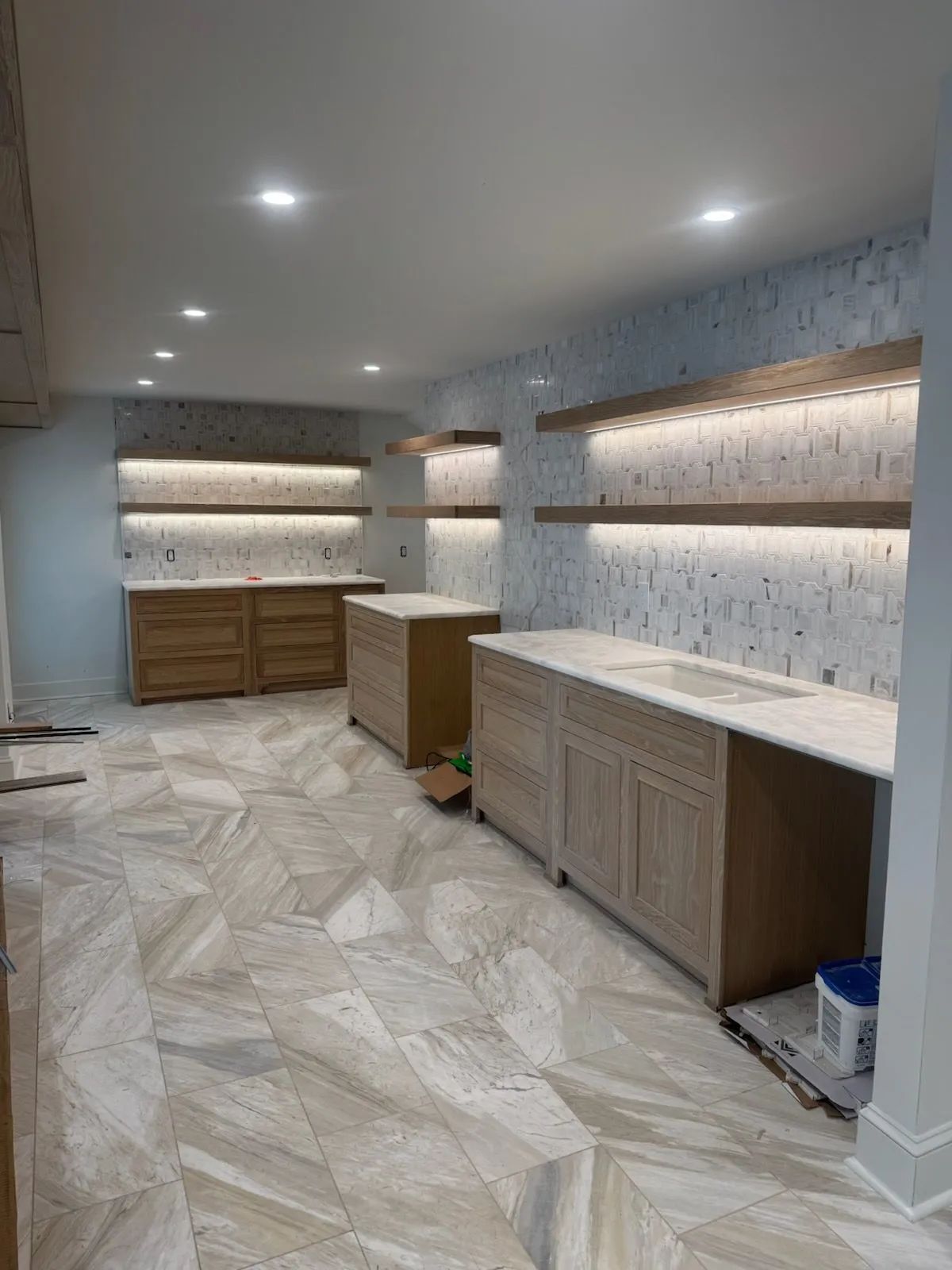 Built-in shelves and cabinets in a modern, empty room with recessed lighting and herringbone tile floor
