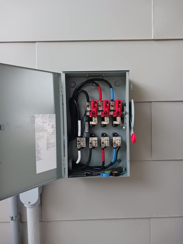 Open electrical panel on a wall. Wires and breakers visible, red and black wires prominent.