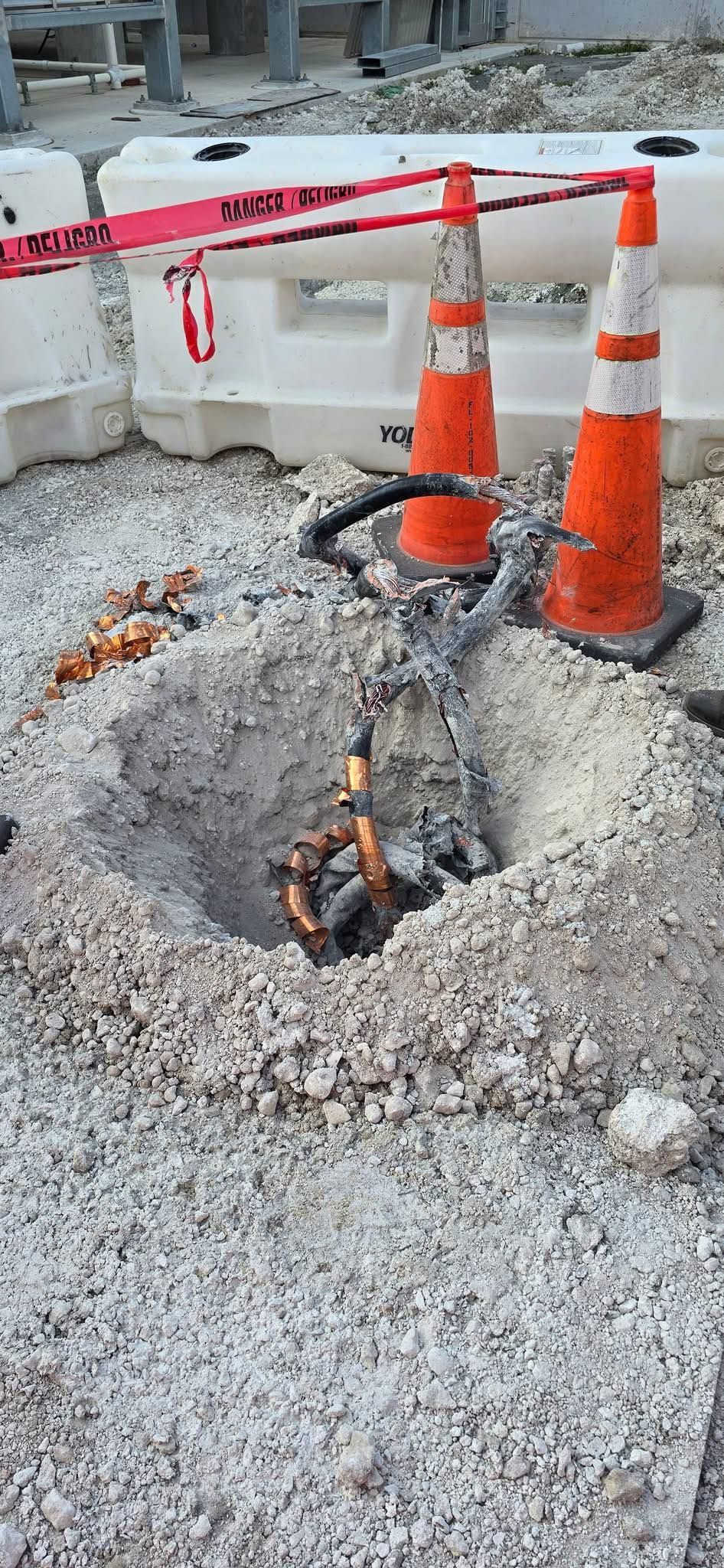 Construction site: hole in ground with debris, orange cones, and caution tape.