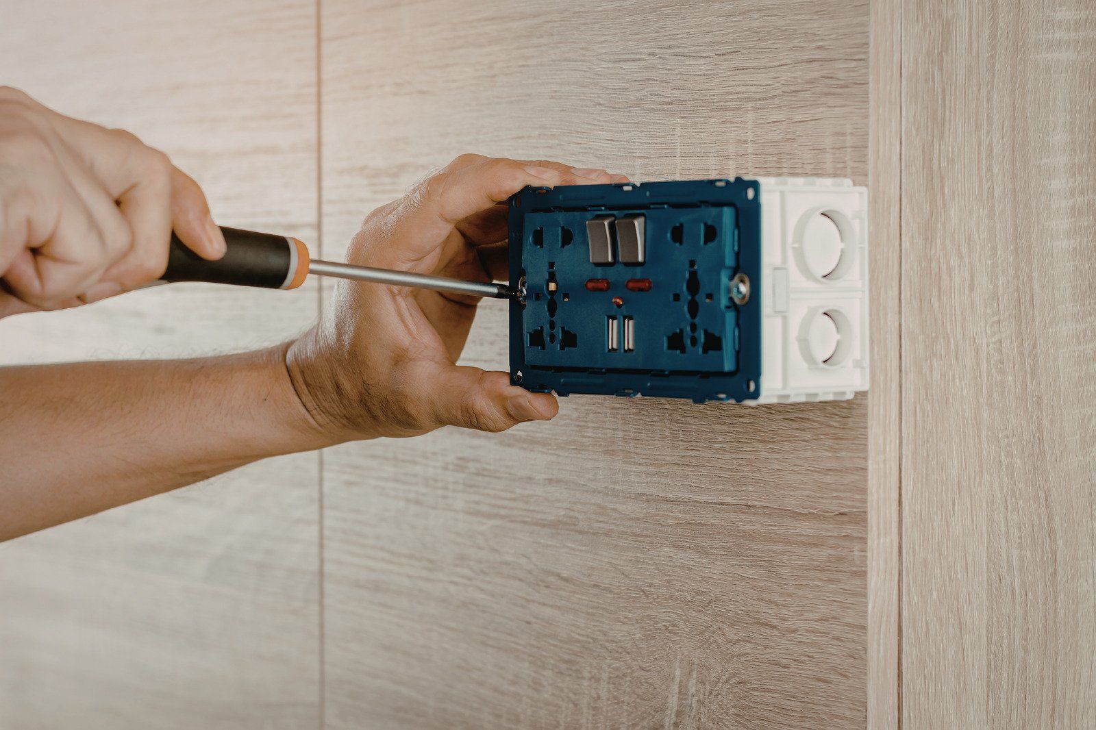Person using a screwdriver to install an electrical outlet box on a wall.