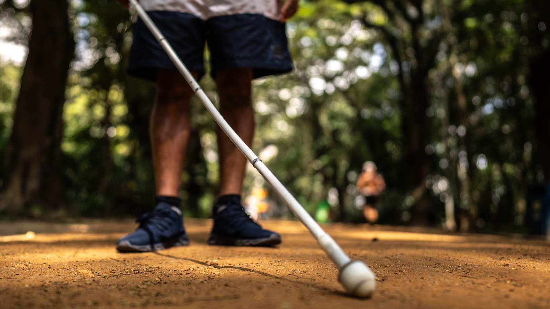 Blindness assistance walking cane mobility device being used by a man in a park