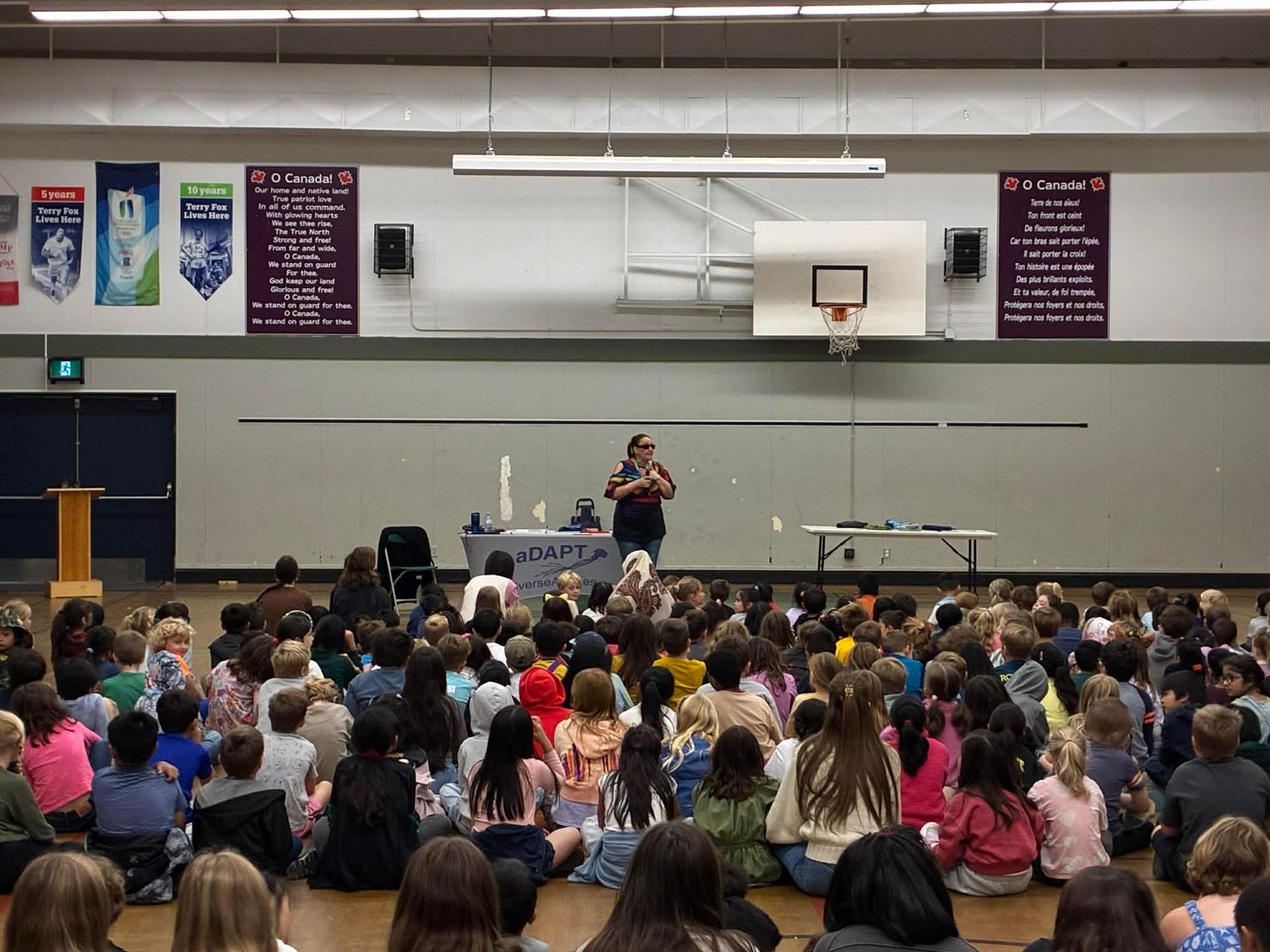 Gina speaking to a school gym full of elementary students for a Youth aDAPT session.
