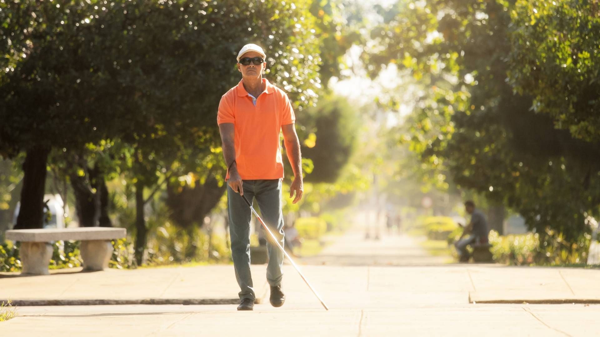 Man with dark glasses on walking through the park with a blindness cane mobility device