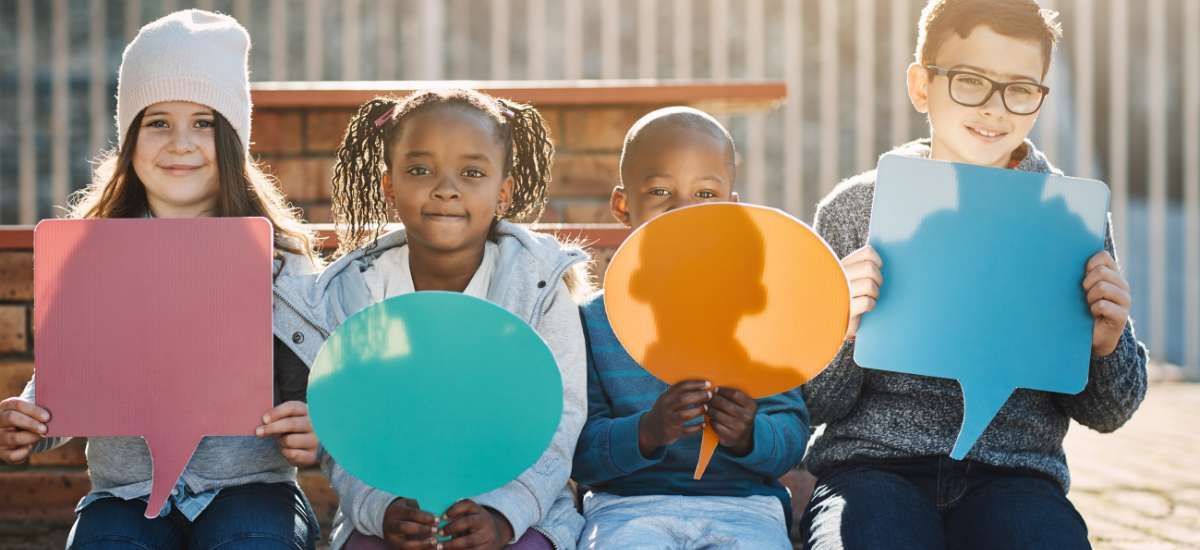4 kids on a bench each holding a different colored speech bubbles without words on them
