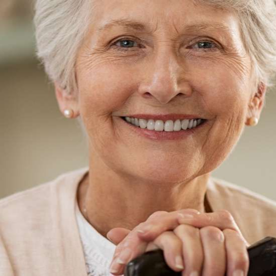 Elderly lady smiling with hands folded on the top of her cane
