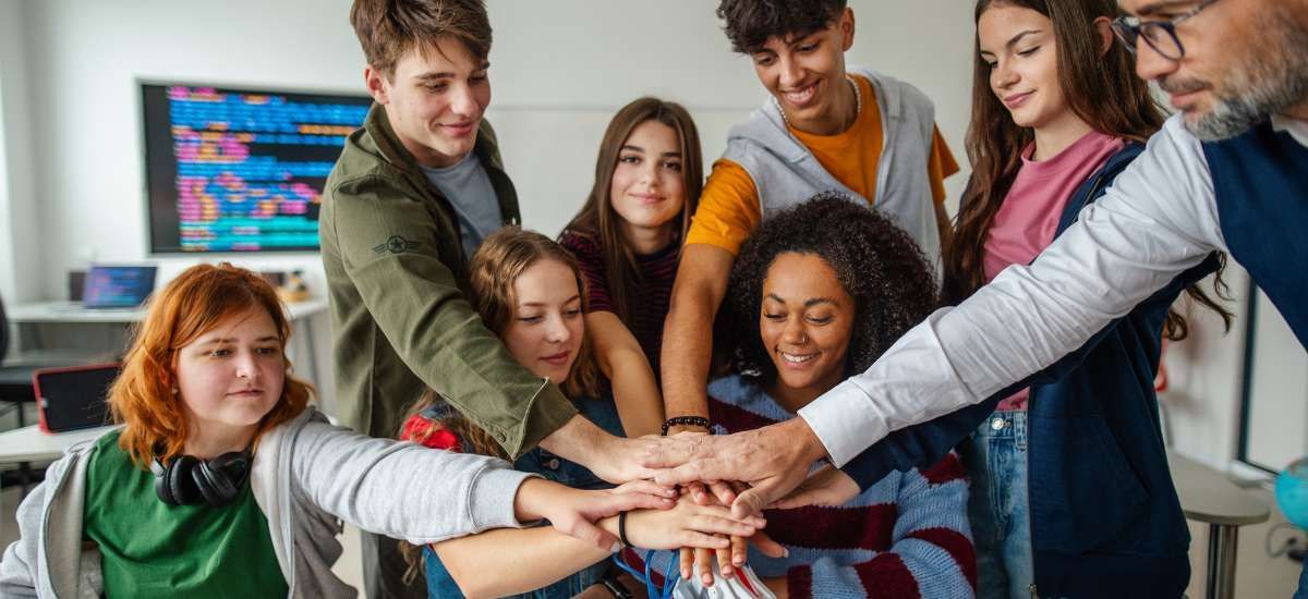 A group of people in post-secondary huddled together with their hands stacked in the middle. Happily working together on a project.