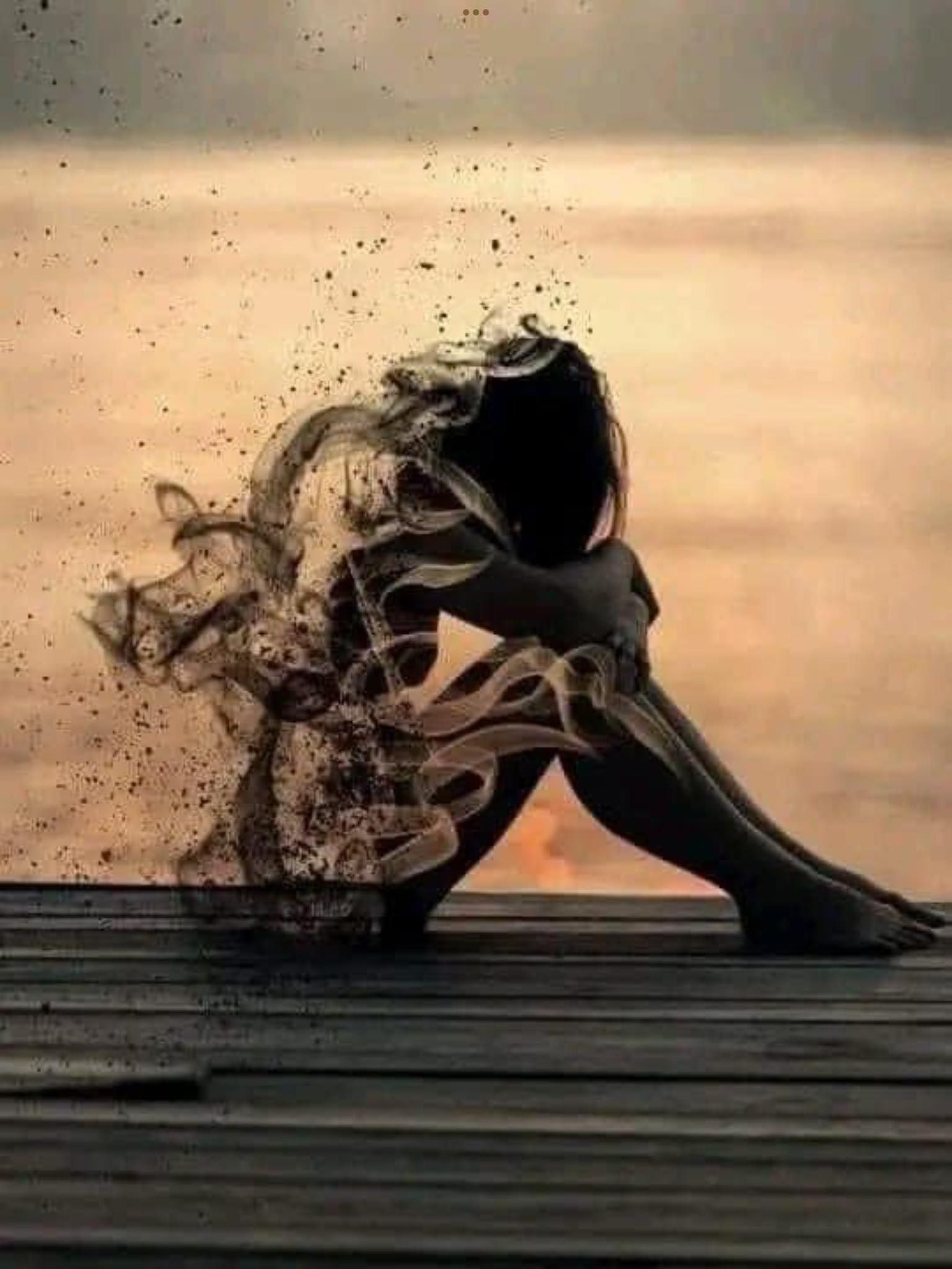 Side view of a person sitting with their head pressed down into crossed arms and holding their knees in while their back fades as if blowing away in the wind.