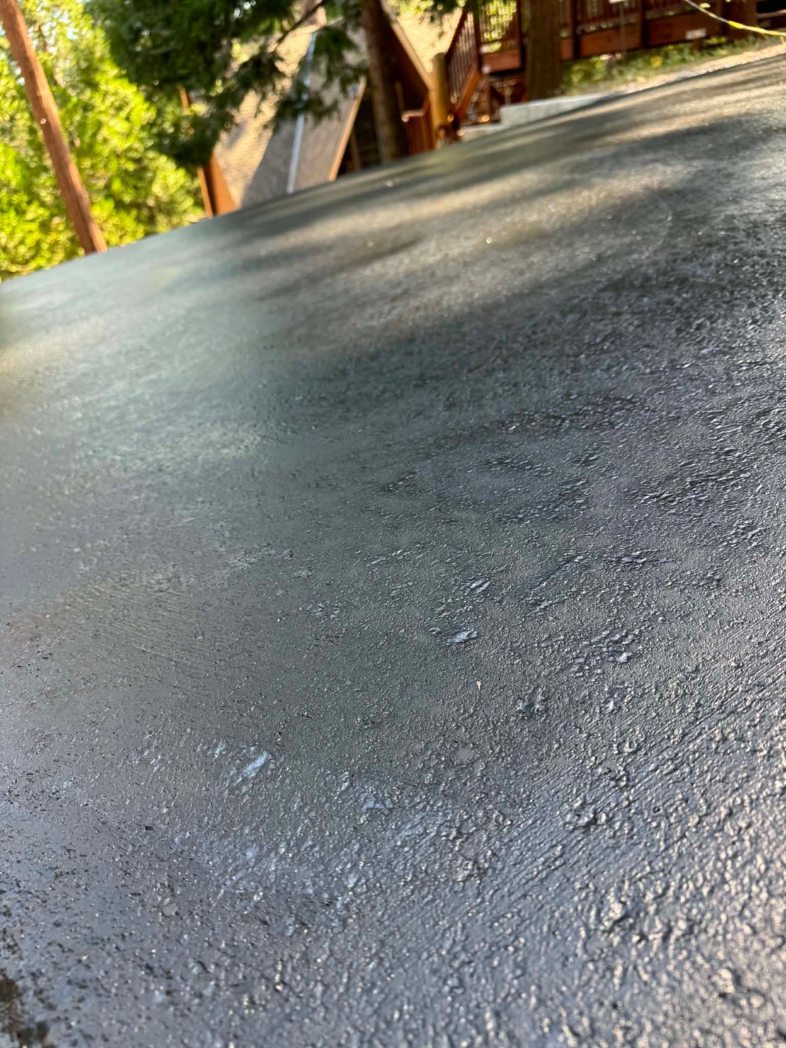 Wet asphalt road with trees and a house in the background, viewed at a slight angle