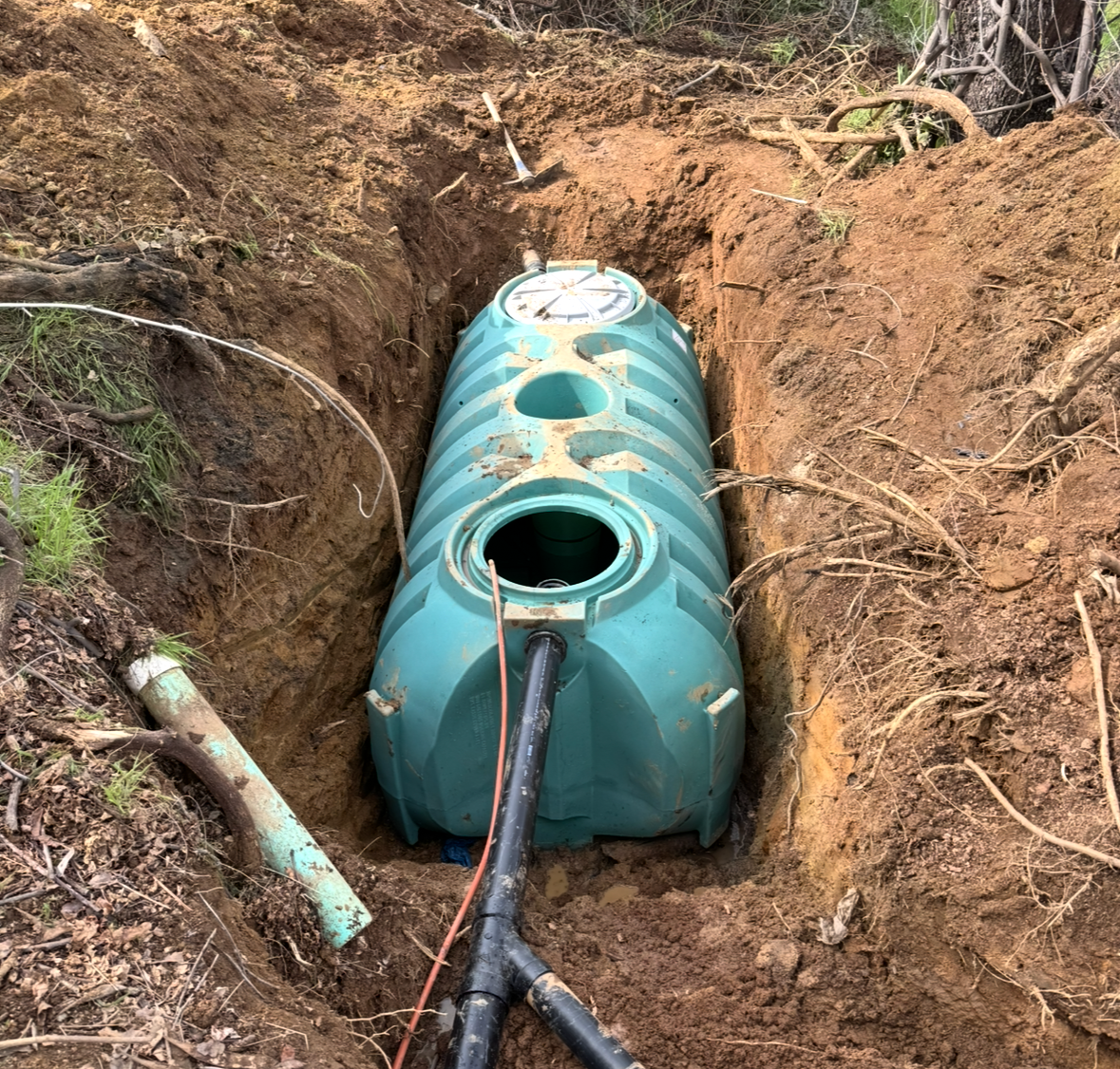 A green septic tank is sitting in a hole in the ground.