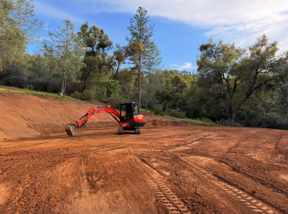 A red excavator is driving through a dirt field.