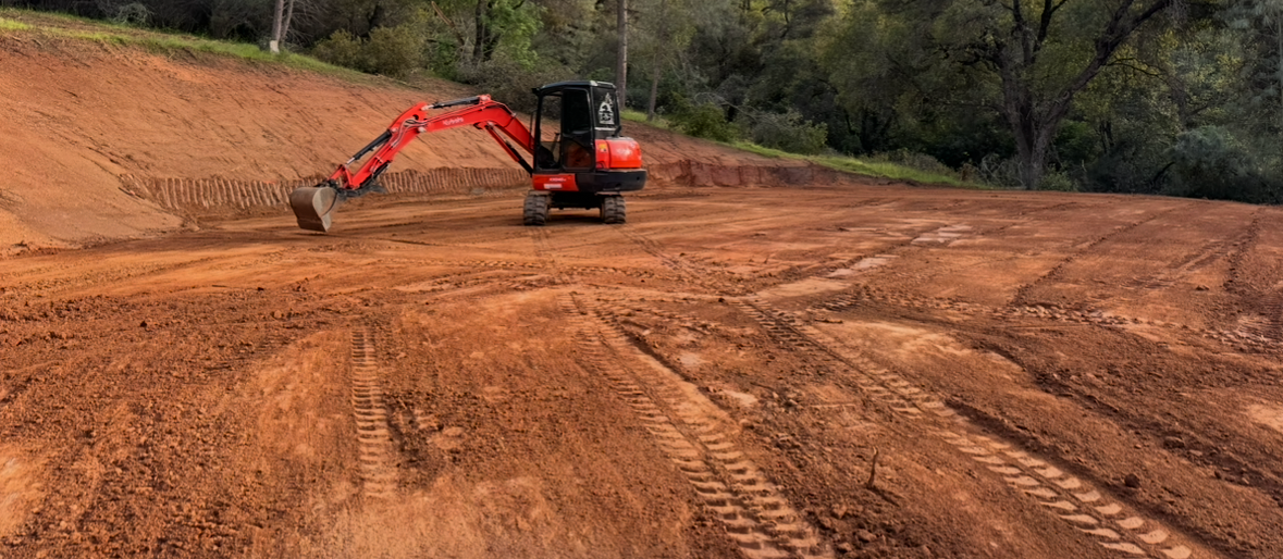 A red excavator is digging a hole in a dirt field.